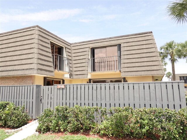 4226 42nd Way, West Palm Beach, FL 33407 - view of property exterior with mansard roof, a balcony, a fenced front yard, stucco siding, and brick siding