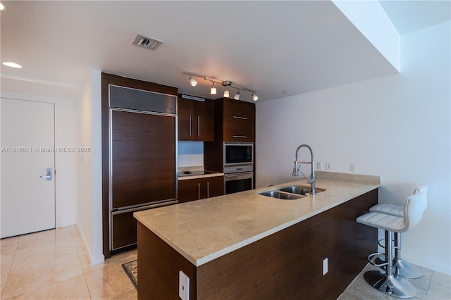 475 Brickell Ave Unit 3512, Miami, FL 33131 - kitchen with a sink, built in appliances, a peninsula, dark brown cabinets, and a kitchen breakfast bar