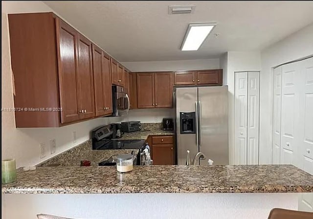11603 NW 89th St Unit 214, Doral, FL 33178 - kitchen featuring stainless steel appliances, a peninsula, stone counters, and brown cabinets