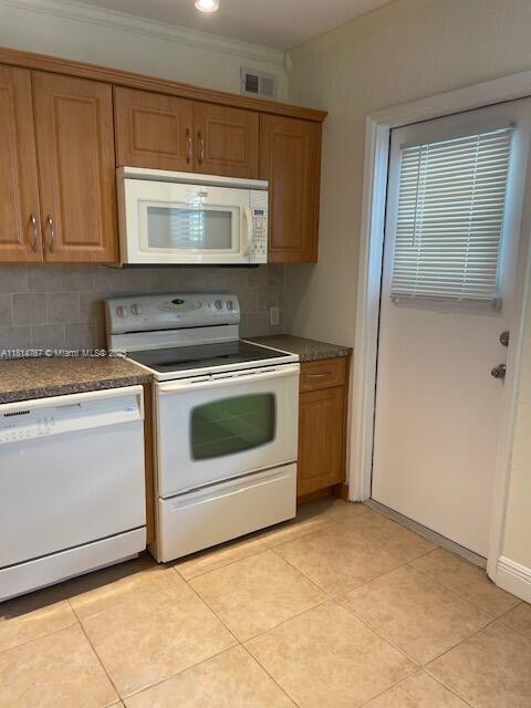 2751 N Palm Aire Dr Unit 504, Pompano Beach, FL 33069 - kitchen with white appliances, decorative backsplash, dark countertops, brown cabinets, and crown molding