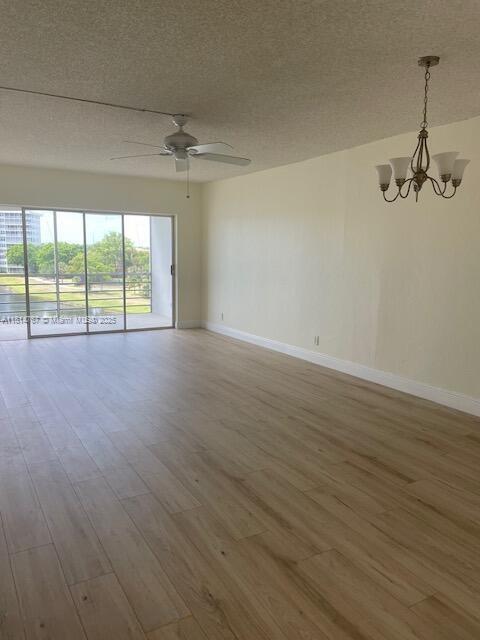 2751 N Palm Aire Dr Unit 504, Pompano Beach, FL 33069 - empty room with wood finished floors, a chandelier, ceiling fan, a textured ceiling, and baseboards