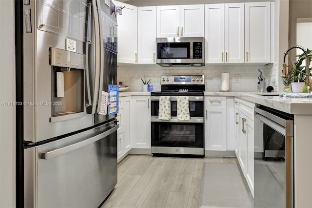 4760 SW 57th Ave, Davie, FL 33314 - kitchen featuring appliances with stainless steel finishes, light wood finished floors, white cabinets, and decorative backsplash