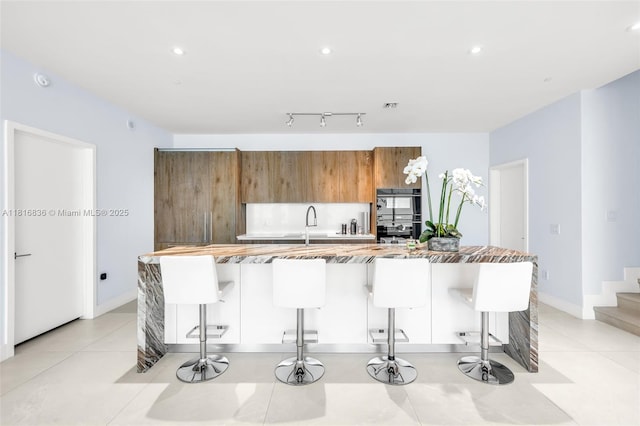 650 NE 32nd St Unit Bh4, Miami, FL 33137 - kitchen with brown cabinetry, a large island, a breakfast bar area, recessed lighting, and light tile patterned floors