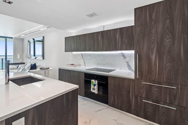 3131 NE 7th Ave Unit 1702, Miami, FL 33137 - kitchen featuring black appliances, modern cabinets, light marble finish floors, dark brown cabinets, and decorative backsplash