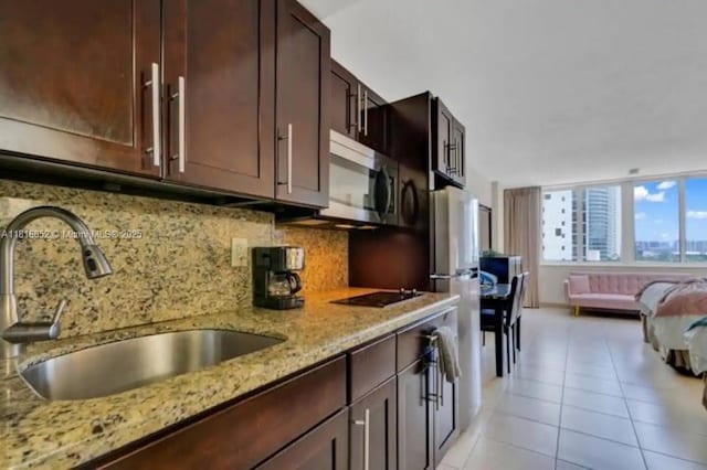 19201 Collins Ave Unit 603, Sunny Isles Beach, FL 33160 - kitchen featuring a sink, stainless steel microwave, decorative backsplash, light stone countertops, and dark brown cabinetry