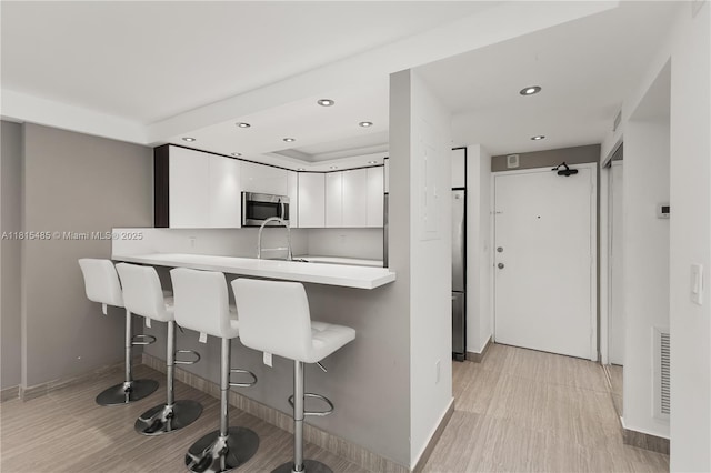 401 Ocean Dr Unit 221, Miami Beach, FL 33139 - kitchen featuring stainless steel appliances, white cabinetry, a kitchen breakfast bar, recessed lighting, and baseboards