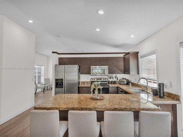 18424 NW 21st St, Pembroke Pines, FL 33029 - kitchen featuring appliances with stainless steel finishes, a peninsula, dark brown cabinetry, a kitchen breakfast bar, and light stone counters