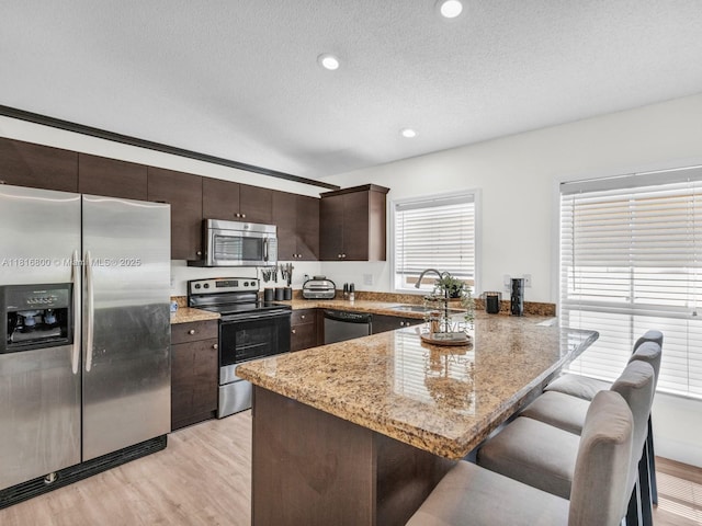 18424 NW 21st St, Pembroke Pines, FL 33029 - kitchen featuring appliances with stainless steel finishes, a sink, a peninsula, dark brown cabinets, and a kitchen breakfast bar