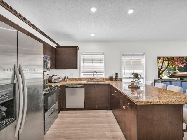 18424 NW 21st St, Pembroke Pines, FL 33029 - kitchen with stainless steel appliances, a sink, a peninsula, dark brown cabinetry, and light wood-style floors