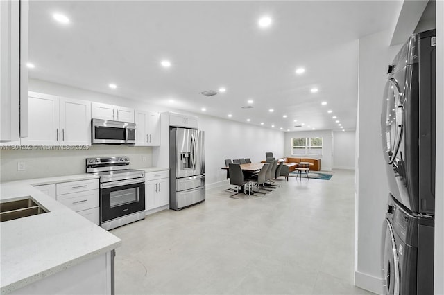 3655 Stirling Rd, Hollywood, FL 33312 - kitchen featuring appliances with stainless steel finishes, stacked washing machine and dryer, recessed lighting, baseboards, and white cabinets