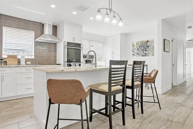1547 NE 38th St, Oakland Park, FL 33334 - kitchen with wall chimney exhaust hood, wood finish floors, backsplash, a breakfast bar, and white cabinetry