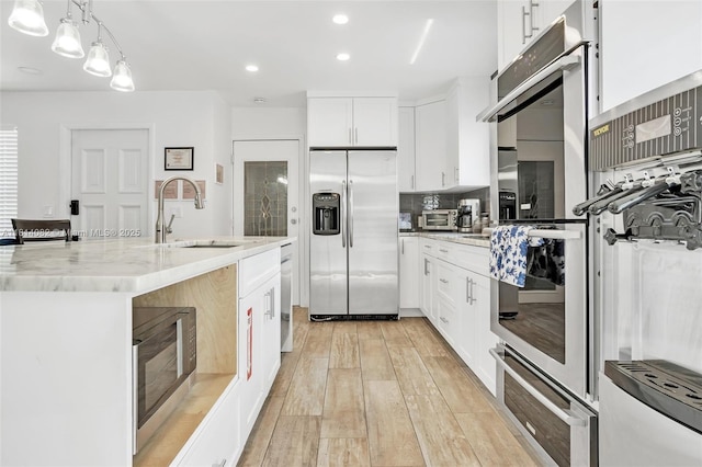 1547 NE 38th St, Oakland Park, FL 33334 - kitchen featuring appliances with stainless steel finishes, a sink, light wood-type flooring, white cabinets, and an island with sink