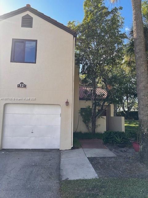 12 Via De Casas Sur Unit 104, Boynton Beach, FL 33426 - view of front of house with a garage, stucco siding, and driveway