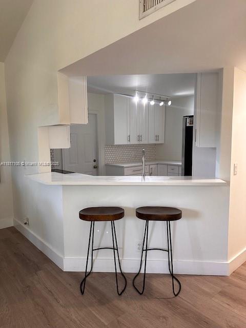 12 Via De Casas Sur Unit 104, Boynton Beach, FL 33426 - kitchen featuring light wood-style flooring, a breakfast bar area, white cabinets, and a peninsula
