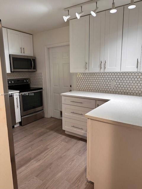 12 Via De Casas Sur Unit 104, Boynton Beach, FL 33426 - kitchen featuring appliances with stainless steel finishes, white cabinets, backsplash, light wood-type flooring, and light countertops