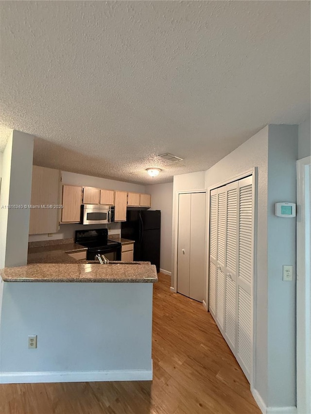 3705SW 27 Th St Unit 416, Gainesville, FL 32608 - kitchen featuring black appliances, a peninsula, a textured ceiling, light brown cabinetry, and light wood finished floors