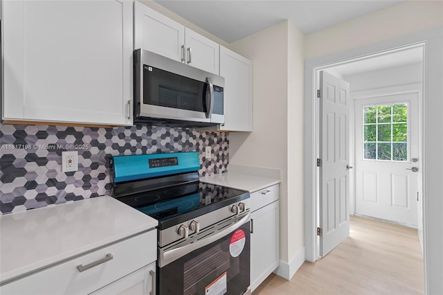 8510 SE Citrus Way, Hobe Sound, FL 33455 - kitchen with appliances with stainless steel finishes, backsplash, light countertops, white cabinetry, and light wood-style flooring
