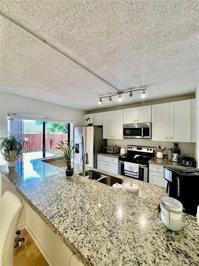 4306 43rd Way, West Palm Beach, FL 33407 - kitchen featuring stainless steel appliances, a sink, white cabinetry, light stone counters, and wood finished floors