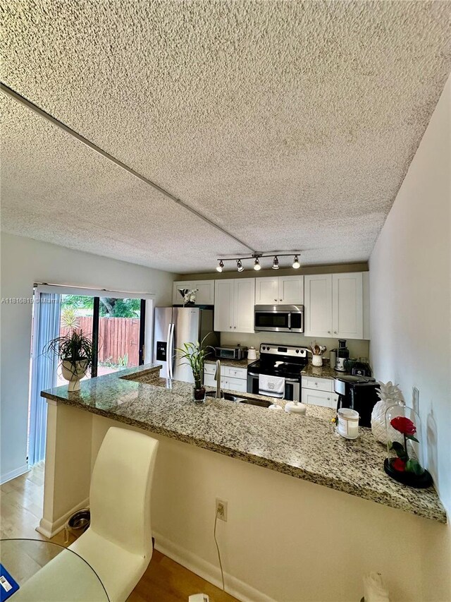 4306 43rd Way, West Palm Beach, FL 33407 - kitchen featuring stainless steel appliances, track lighting, a peninsula, white cabinetry, and stone countertops