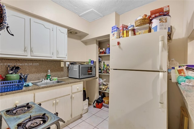 1478 SW 2nd St, Miami, FL 33135 - kitchen featuring freestanding refrigerator, stainless steel microwave, white cabinets, light tile patterned flooring, and a sink