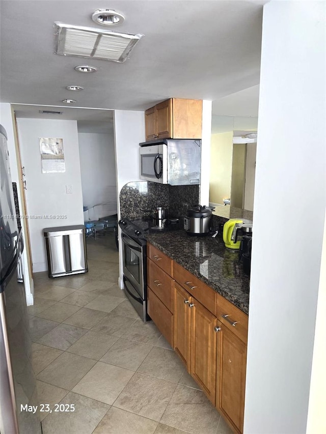 230 174th St Unit 1805, Sunny Isles Beach, FL 33160 - kitchen with stainless steel appliances, brown cabinetry, dark stone countertops, decorative backsplash, and light tile patterned flooring