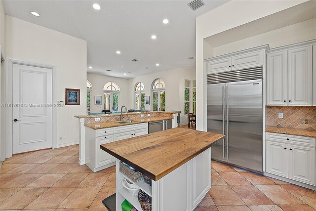 112 Segovia Way, Jupiter, FL 33458 - kitchen with appliances with stainless steel finishes, a kitchen island with sink, wood counters, a sink, and tasteful backsplash