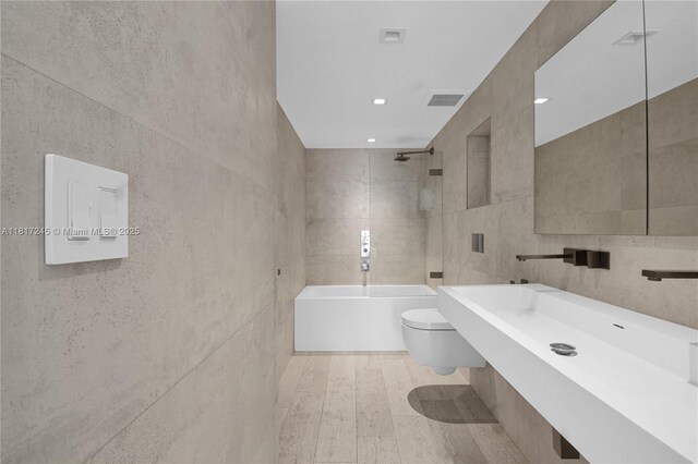 5700 Collins Ave Unit 7A, Miami Beach, FL 33140 - bathroom with tile walls, toilet, washtub / shower combination, and wood finished floors