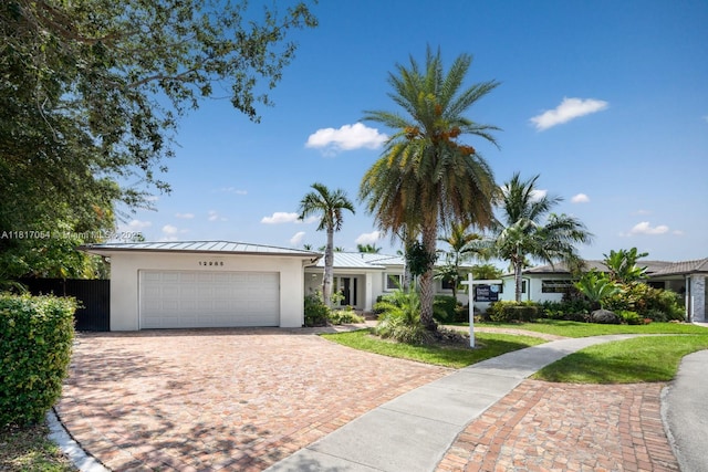 12985 Ortega Ln, North Miami, FL 33181 - view of front of home featuring a standing seam roof, stucco siding, an attached garage, metal roof, and driveway
