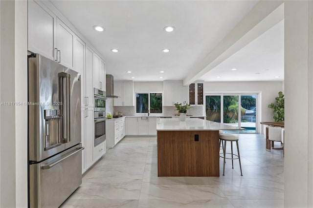 12985 Ortega Ln, North Miami, FL 33181 - kitchen with high quality fridge, healthy amount of natural light, wall chimney exhaust hood, a kitchen island, and recessed lighting