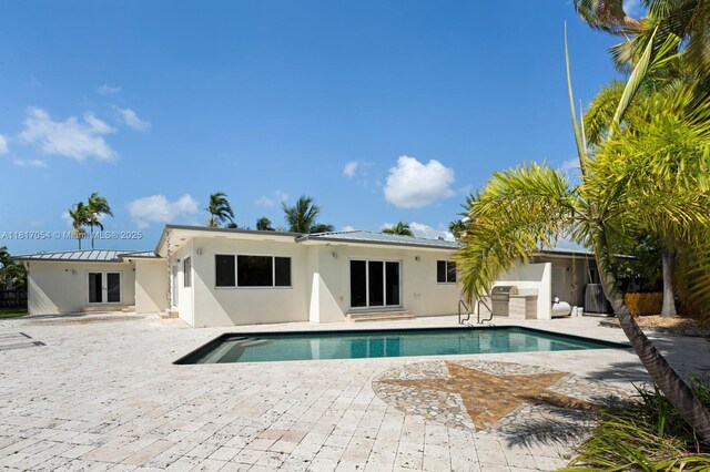 12985 Ortega Ln, North Miami, FL 33181 - rear view of house with stucco siding, a patio area, metal roof, and an outdoor pool