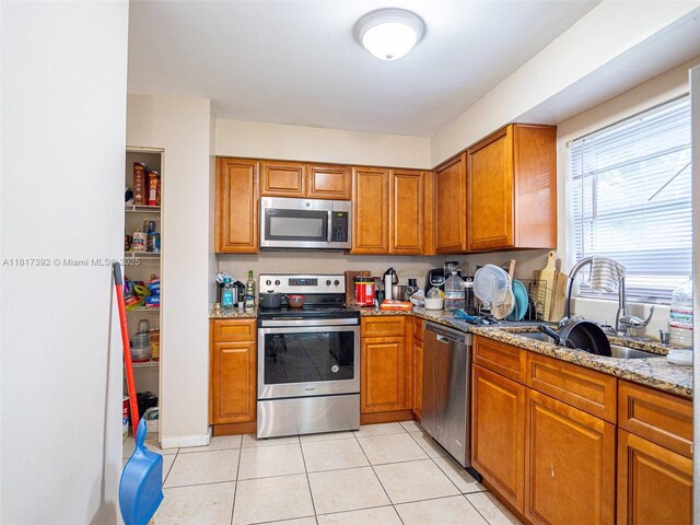 4915 Pine Needle Dr, Orlando, FL 32808 - kitchen with stainless steel appliances, a sink, brown cabinets, light stone counters, and light tile patterned flooring