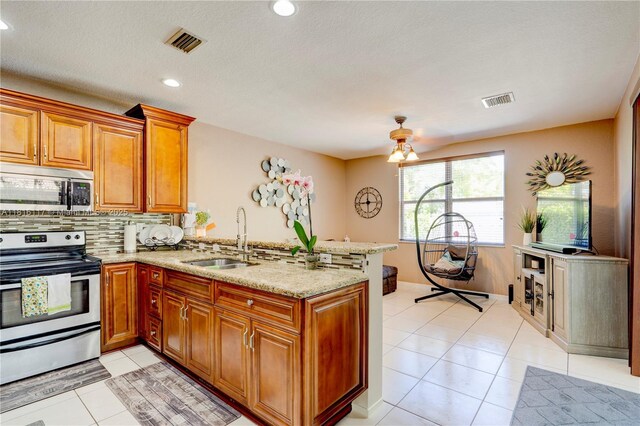 1100 SE 19th Ave, Homestead, FL 33035 - kitchen featuring appliances with stainless steel finishes, a peninsula, backsplash, brown cabinets, and light stone countertops