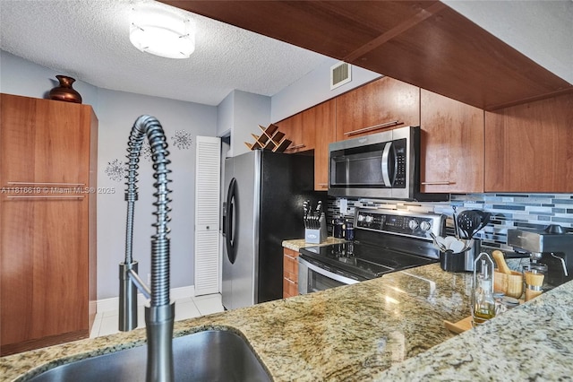 14001 SW 91st Ter Unit 14001, Miami, FL 33186 - kitchen with appliances with stainless steel finishes, brown cabinets, decorative backsplash, light stone counters, and a textured ceiling