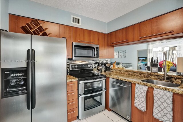 14001 SW 91st Ter Unit 14001, Miami, FL 33186 - kitchen featuring stainless steel appliances, brown cabinetry, a sink, light stone countertops, and light tile patterned floors