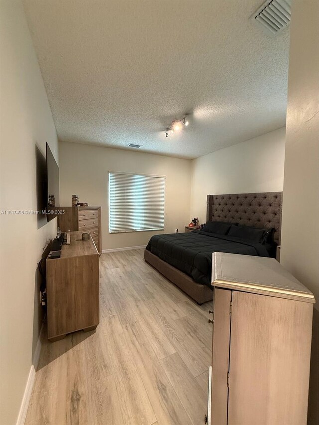 2046 NE 4th Ct, Homestead, FL 33033 - bedroom featuring light wood-style floors, a textured ceiling, baseboards, and rail lighting
