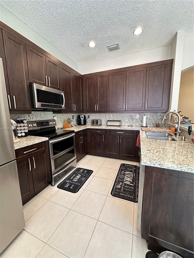 2046 NE 4th Ct, Homestead, FL 33033 - kitchen featuring stainless steel appliances, a sink, light tile patterned flooring, light stone countertops, and a textured ceiling