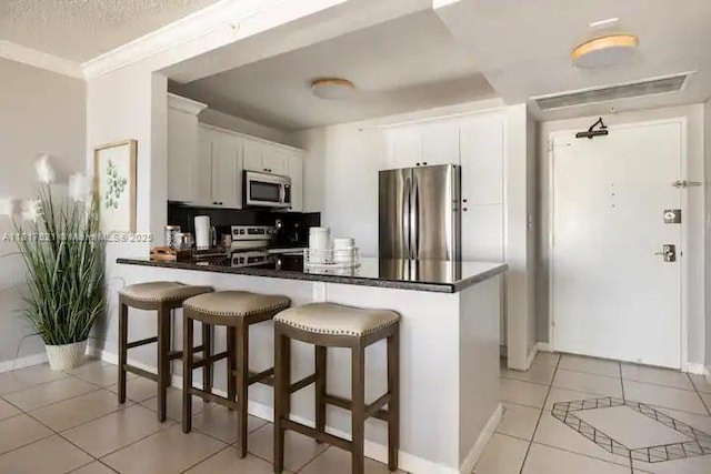 5601 Collins Ave Unit 923, Miami Beach, FL 33140 - kitchen with stainless steel appliances, a peninsula, light tile patterned floors, dark countertops, and a breakfast bar area