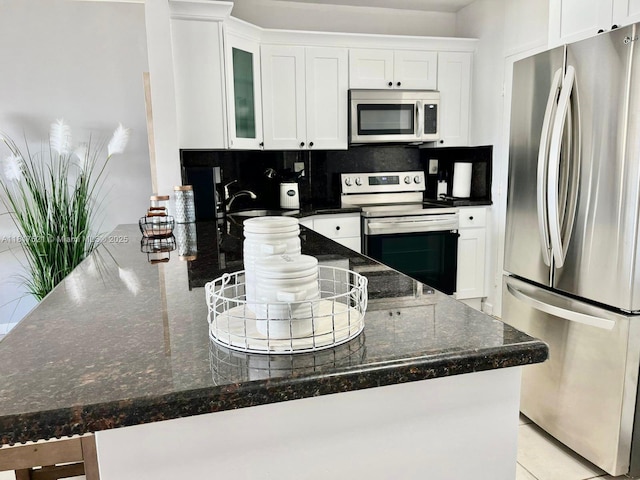 5601 Collins Ave Unit 923, Miami Beach, FL 33140 - kitchen with stainless steel appliances, backsplash, white cabinetry, and glass insert cabinets