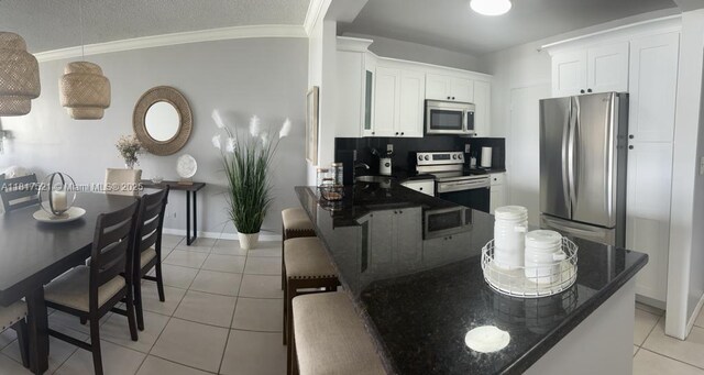 5601 Collins Ave Unit 923, Miami Beach, FL 33140 - kitchen with appliances with stainless steel finishes, light tile patterned floors, ornamental molding, white cabinets, and baseboards