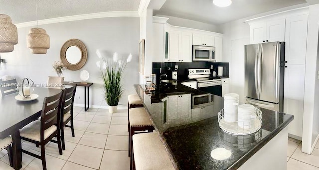 5601 Collins Ave Unit 923, Miami Beach, FL 33140 - kitchen featuring stainless steel appliances, light tile patterned floors, white cabinets, ornamental molding, and dark stone countertops