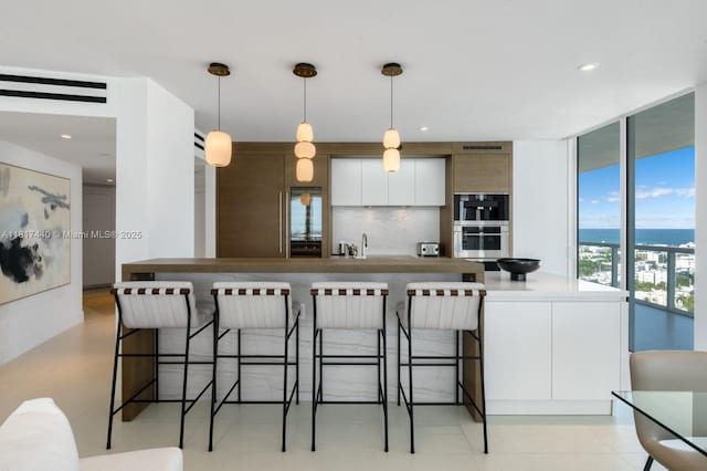 450 Alton Rd Unit 2007, Miami Beach, FL 33139 - kitchen featuring modern cabinets, pendant lighting, a kitchen bar, white cabinetry, and expansive windows