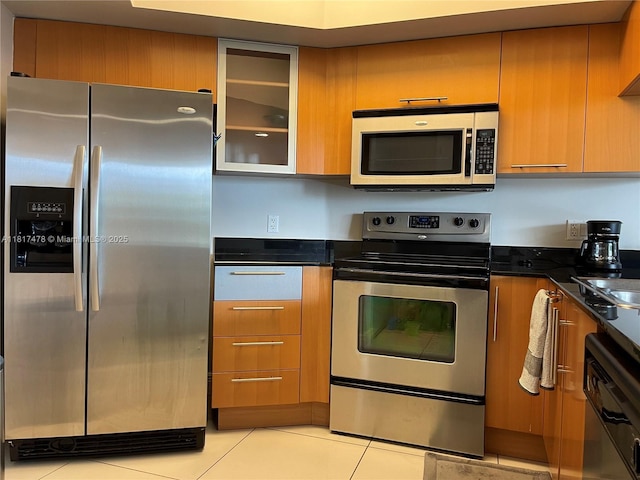 1750 N Bayshore Dr Unit 1414, Miami, FL 33132 - kitchen with appliances with stainless steel finishes, light tile patterned floors, glass insert cabinets, brown cabinetry, and dark stone countertops