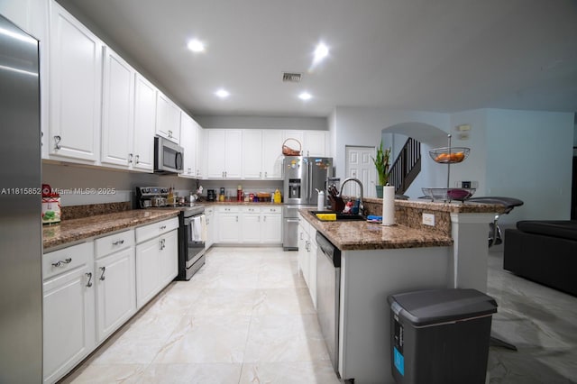 4452 Rainbow Ave, Weston, FL 33332 - kitchen with stainless steel appliances, arched walkways, a center island with sink, a breakfast bar, and white cabinetry
