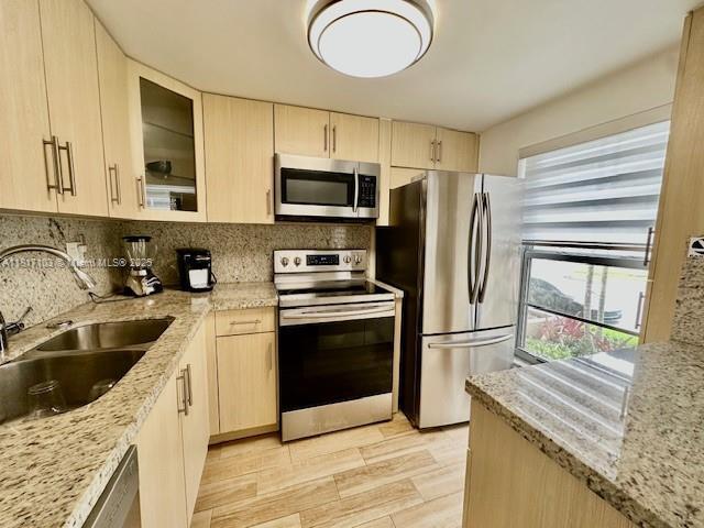 110 Salamanca Ave Unit 207, Coral Gables, FL 33134 - kitchen featuring stainless steel appliances, light brown cabinets, backsplash, light stone countertops, and glass insert cabinets