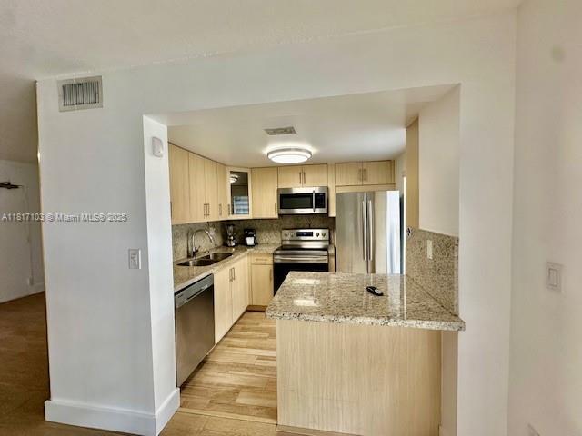 110 Salamanca Ave Unit 207, Coral Gables, FL 33134 - kitchen with stainless steel appliances, light brown cabinets, a sink, tasteful backsplash, and light stone countertops
