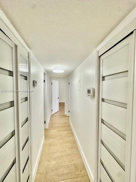 110 Salamanca Ave Unit 207, Coral Gables, FL 33134 - hall with light wood-style floors, baseboards, and a textured ceiling