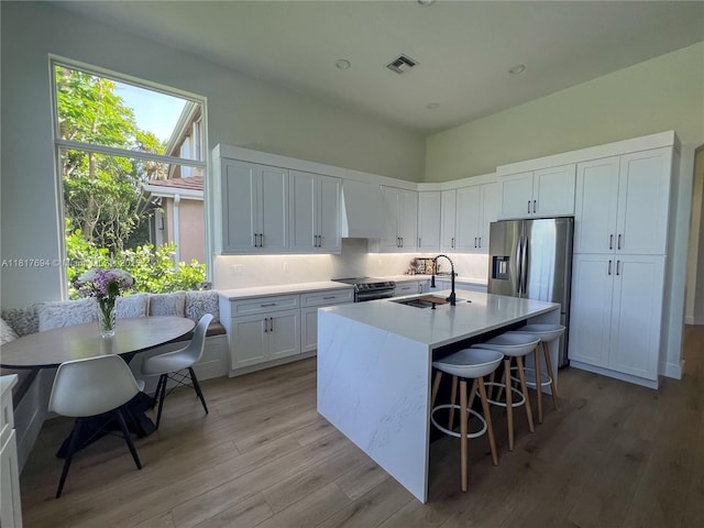7714 NW 70th Way, Parkland, FL 33067 - kitchen with stainless steel fridge with ice dispenser, light wood-style flooring, light countertops, a kitchen island with sink, and white cabinets