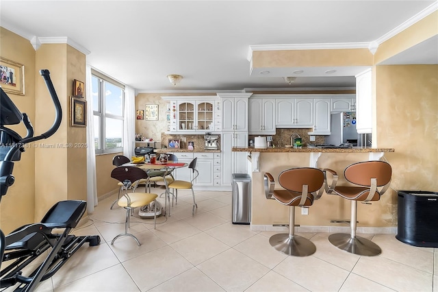 250 174th St Unit 1704, Sunny Isles Beach, FL 33160 - kitchen with decorative backsplash, glass insert cabinets, a breakfast bar, white cabinetry, and crown molding