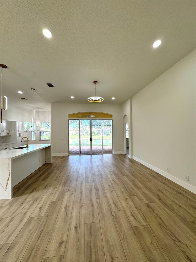 7020 Demedici Cir, Delray Beach, FL 33446 - unfurnished living room with light wood finished floors, recessed lighting, arched walkways, and a textured ceiling