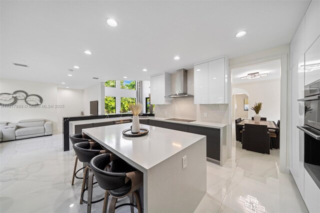 3461 SW 145th Ave, Miramar, FL 33027 - kitchen featuring wall chimney range hood, modern cabinets, black electric stovetop, a breakfast bar area, and white cabinetry